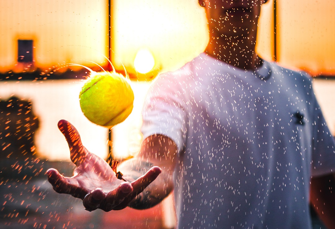 Athlete tossing a tennis ball at sunset