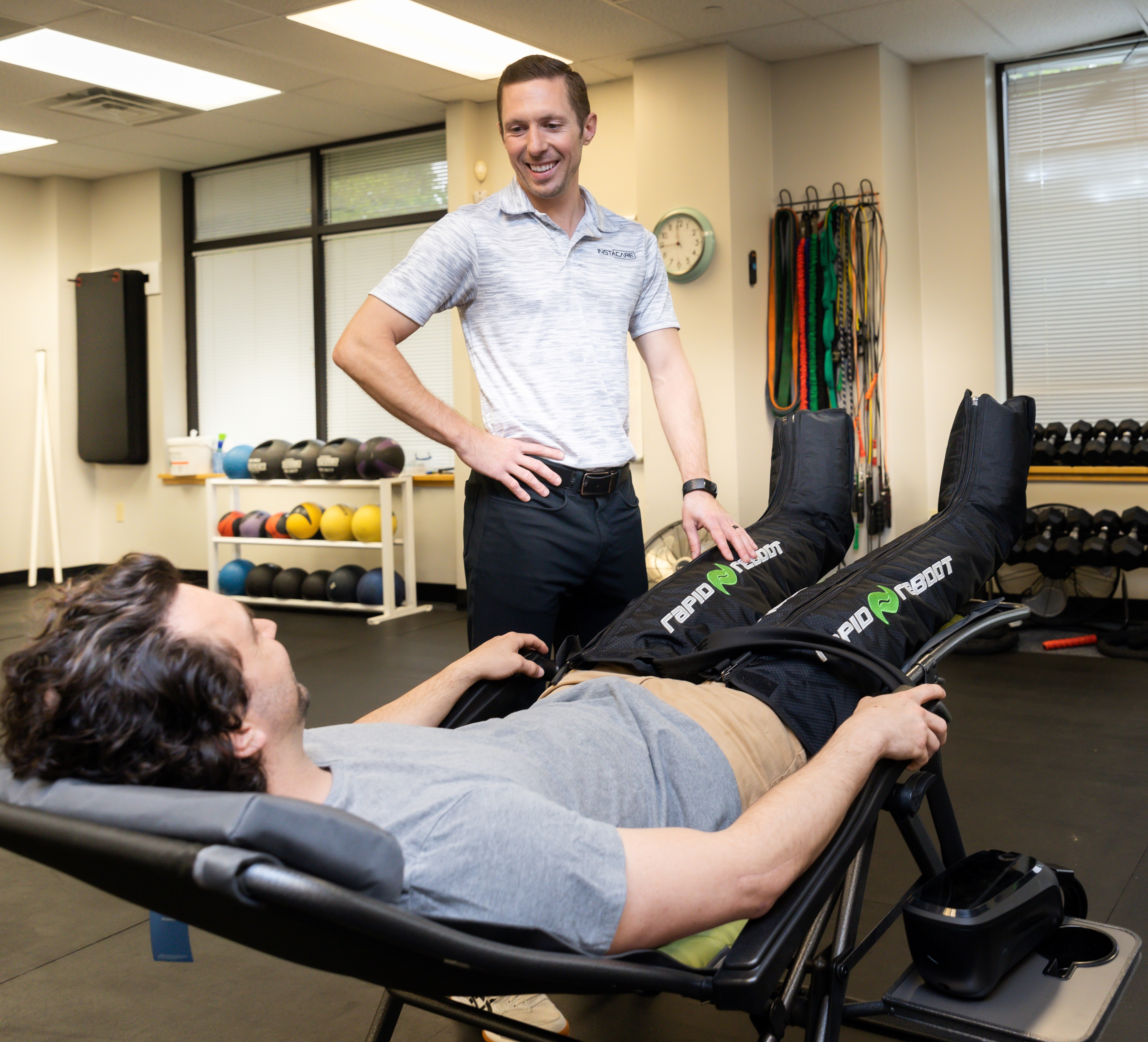 Patient using compression recovery boots while a physical therapist looks on