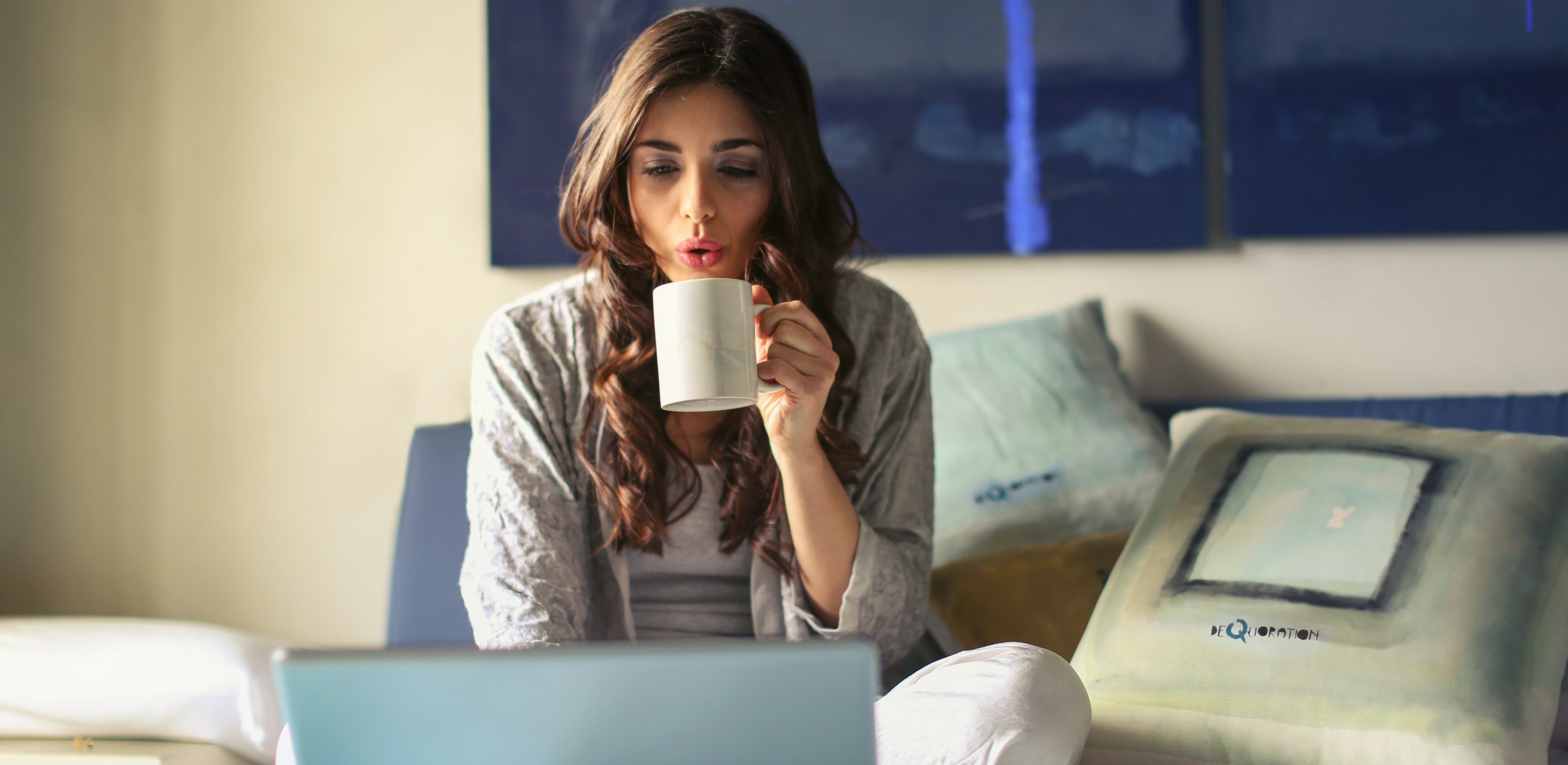 Woman sipping coffee while working from home on a laptop